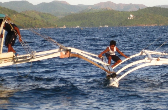 Outriggers equal stability. This man is tying two boats together using their outriggers to keep them stable while anchored. 